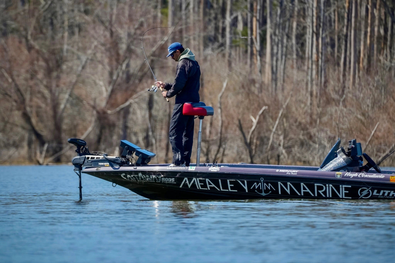 Side shot of a fisherman on a bass boat with the words Mealey Marine written on the side of the bass boat. 